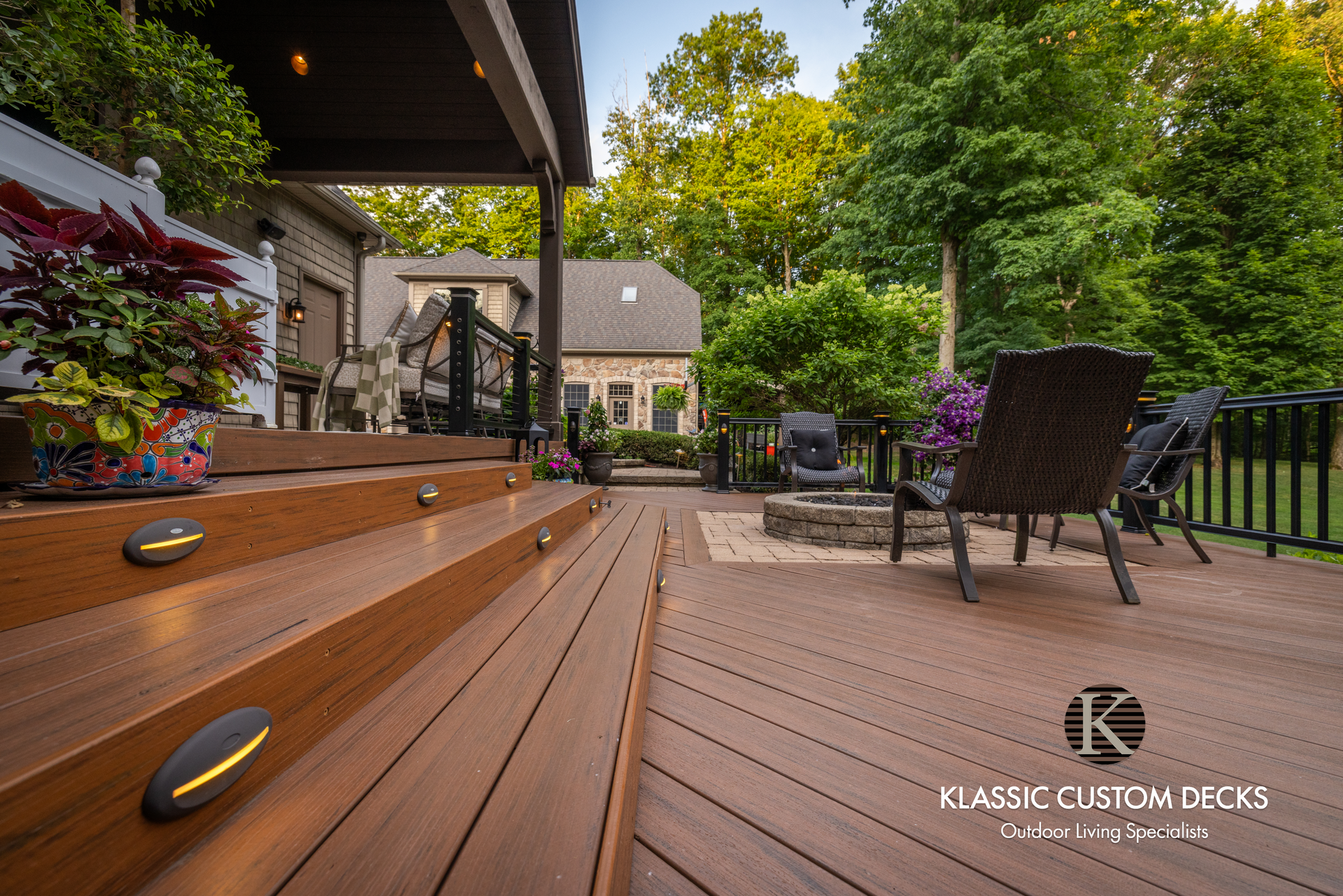 Wooden deck with steps, patio chairs, and a landscaped backyard at dusk
