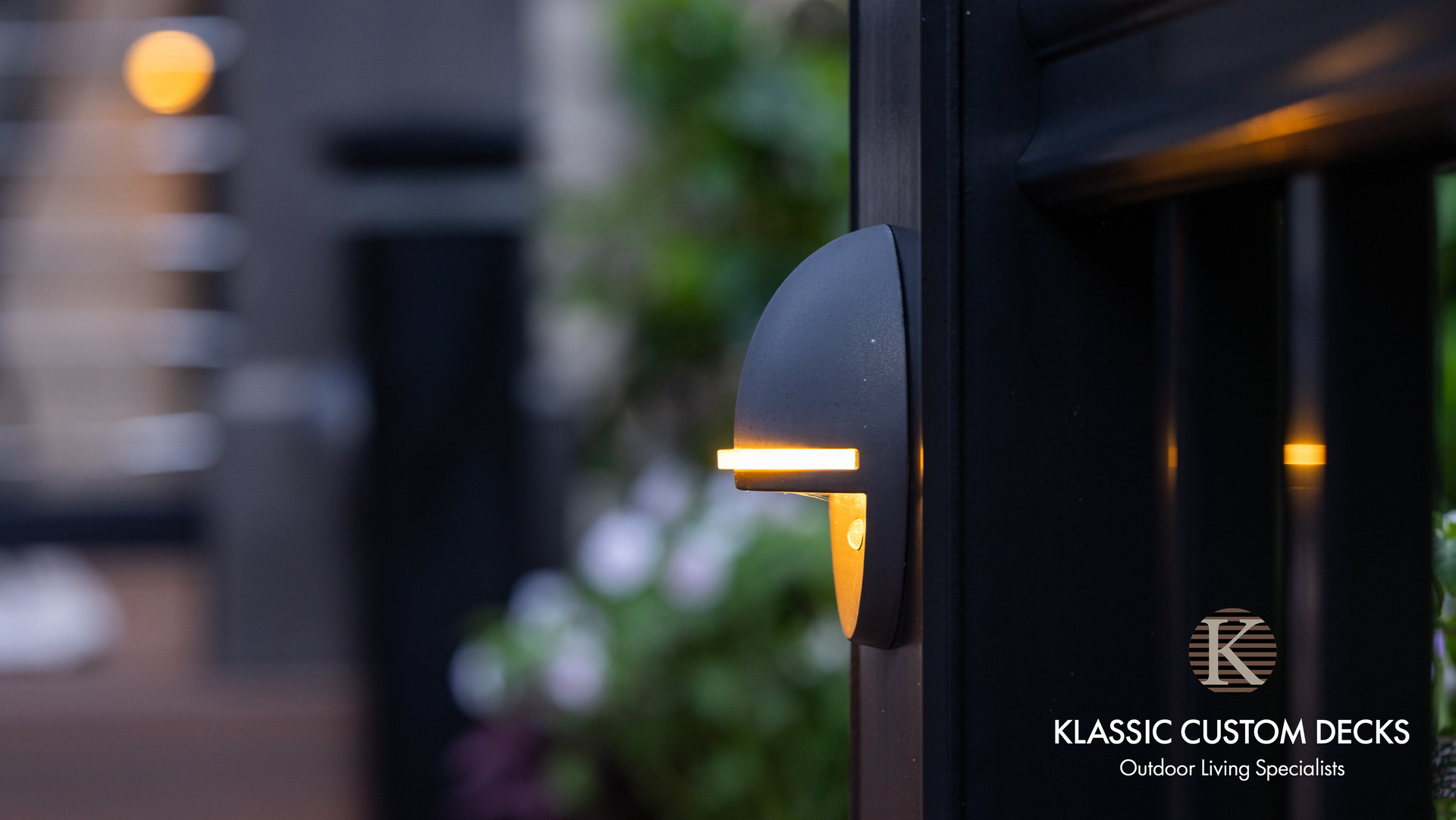 Close-up of a black wall light glowing warmly on a dark exterior wall at dusk