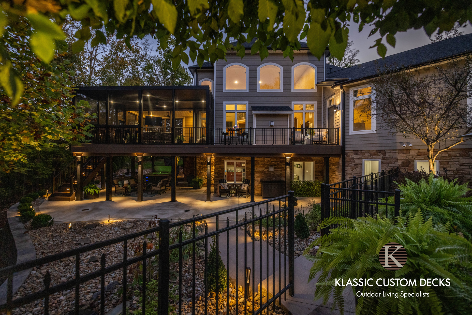Large modern house with warm lit windows and a black fence at dusk