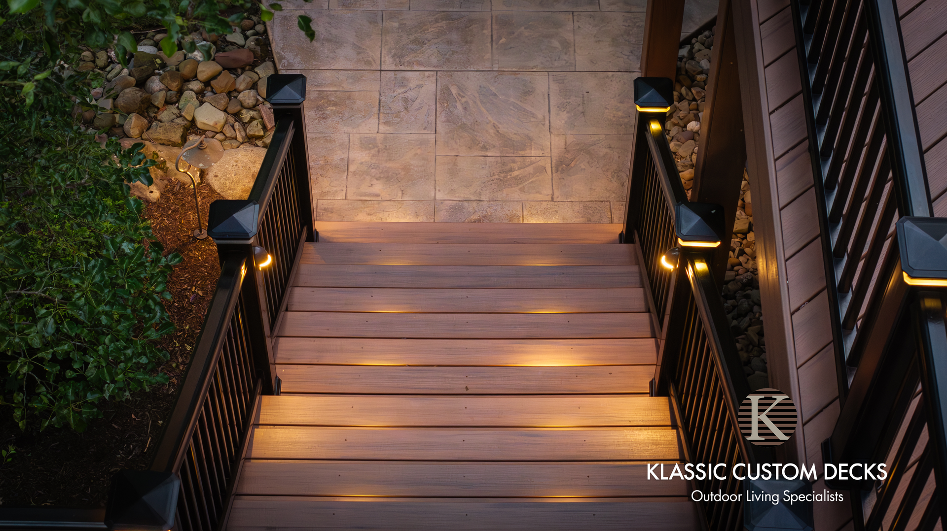 Lit stone staircase with black railings and warm pathway lights leading to a stone patio at dusk