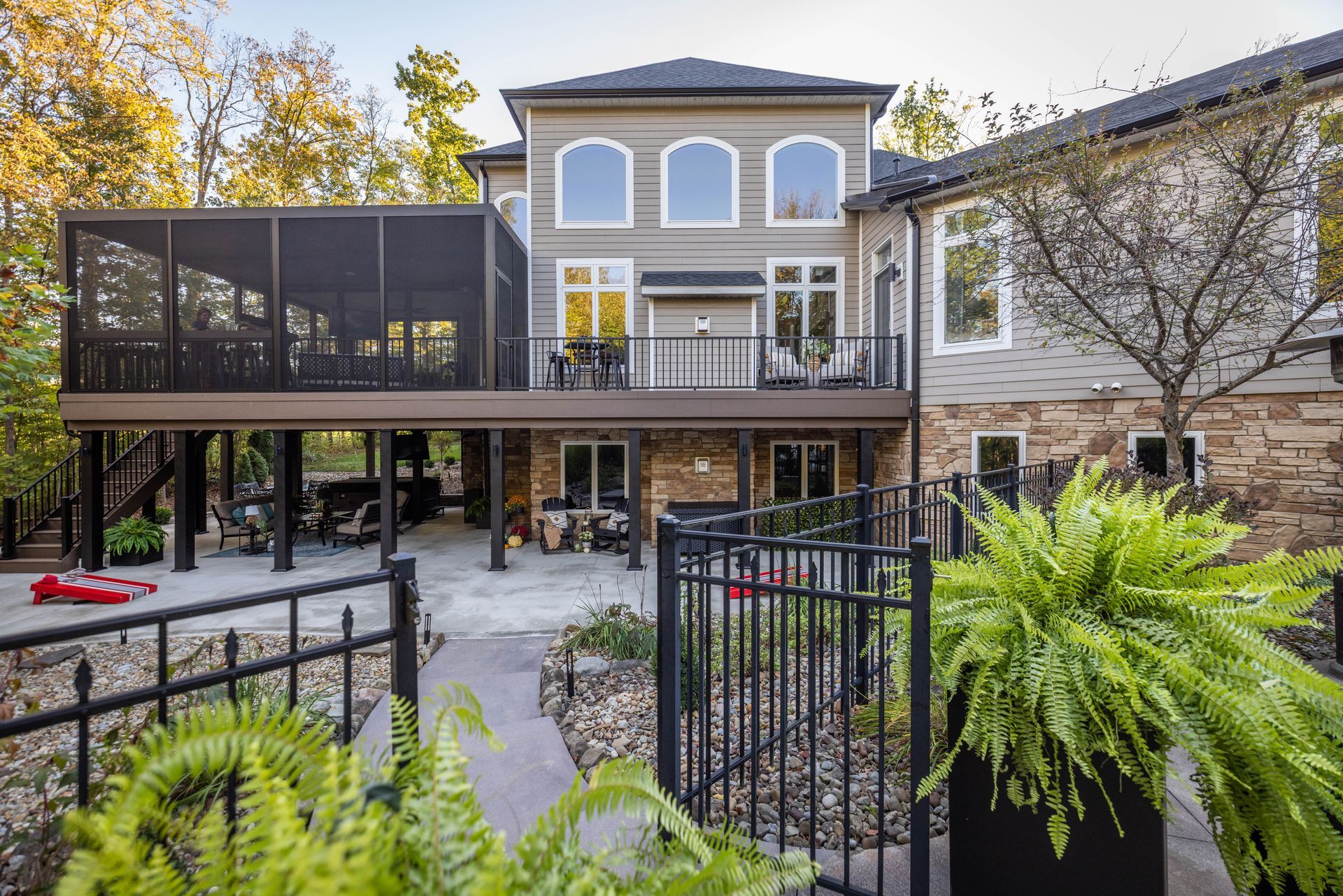 Modern two-story house with deck, black railing, and lush green courtyard garden