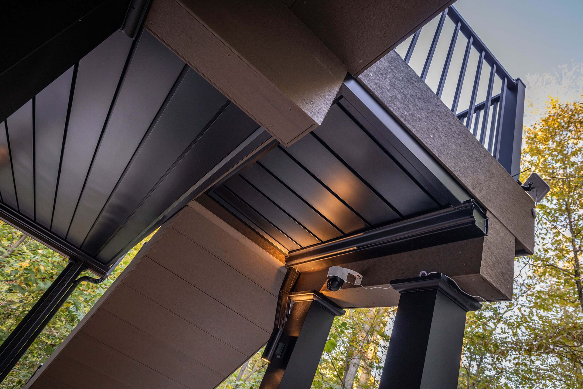 Modern outdoor staircase with dark railings and wood paneling, viewed from below amid trees.