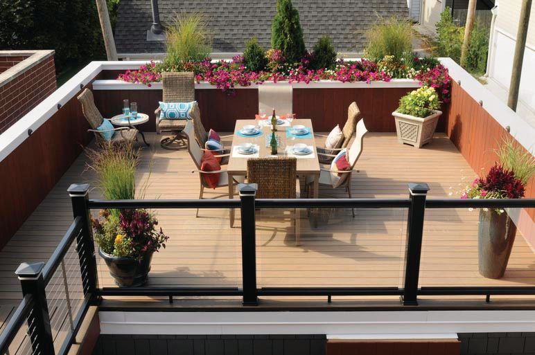 Outdoor patio with wooden deck, dining table, chairs, potted flowers, and black railing