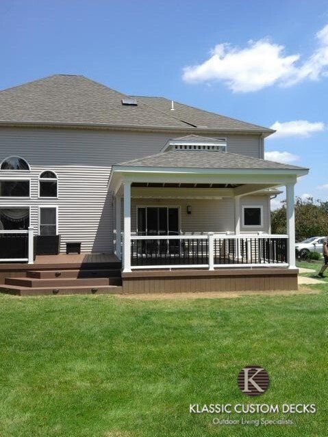 Backyard deck with white railing and roofed cover attached to a gray house under a blue sky