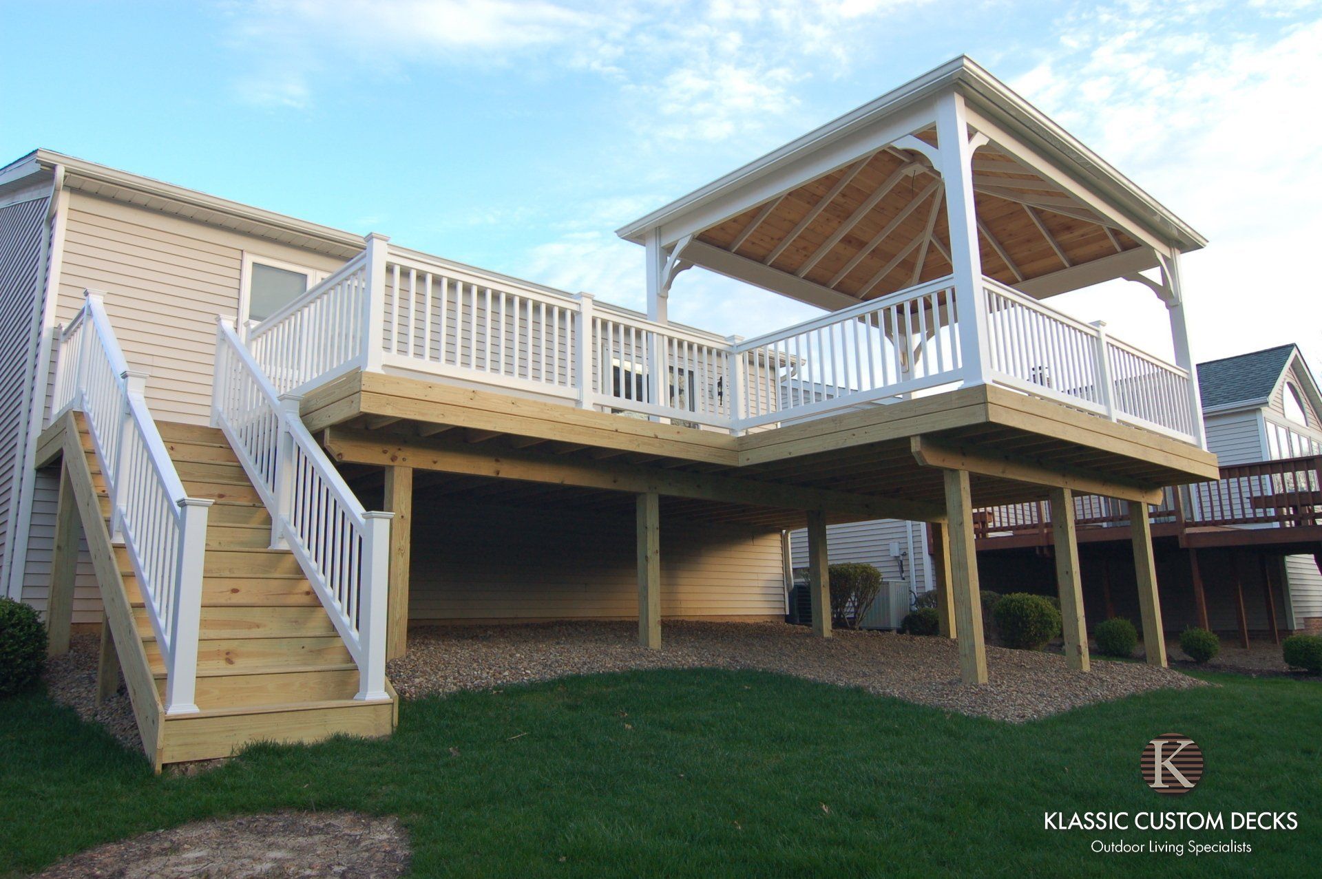 Covered deck with white railings and stairs on a raised home, with a screened gazebo on the right.