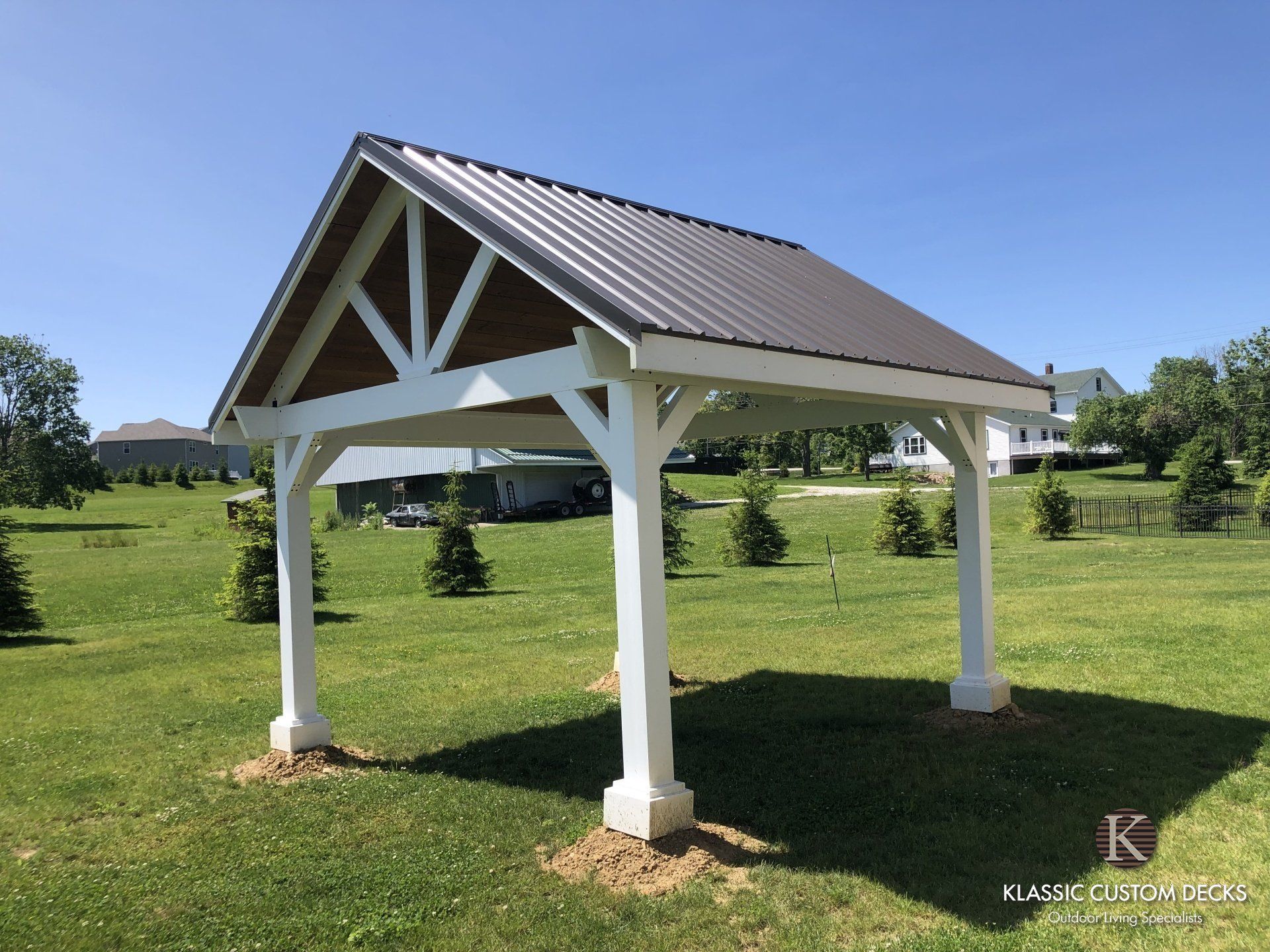 White gazebo with a brown roof in a grassy park under a blue sky