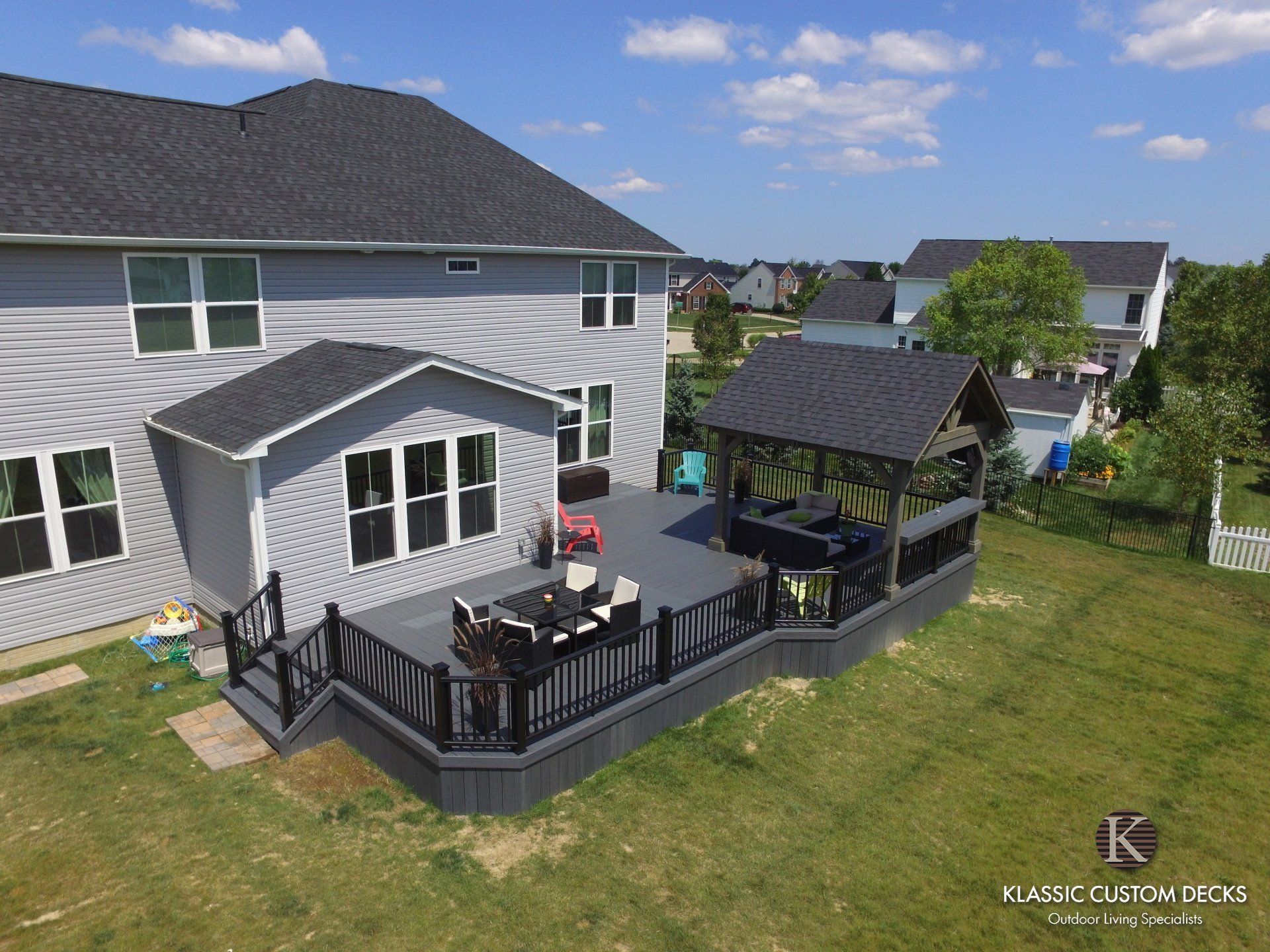 Suburban backyard with raised deck, outdoor seating, and a covered gazebo beside a gray house