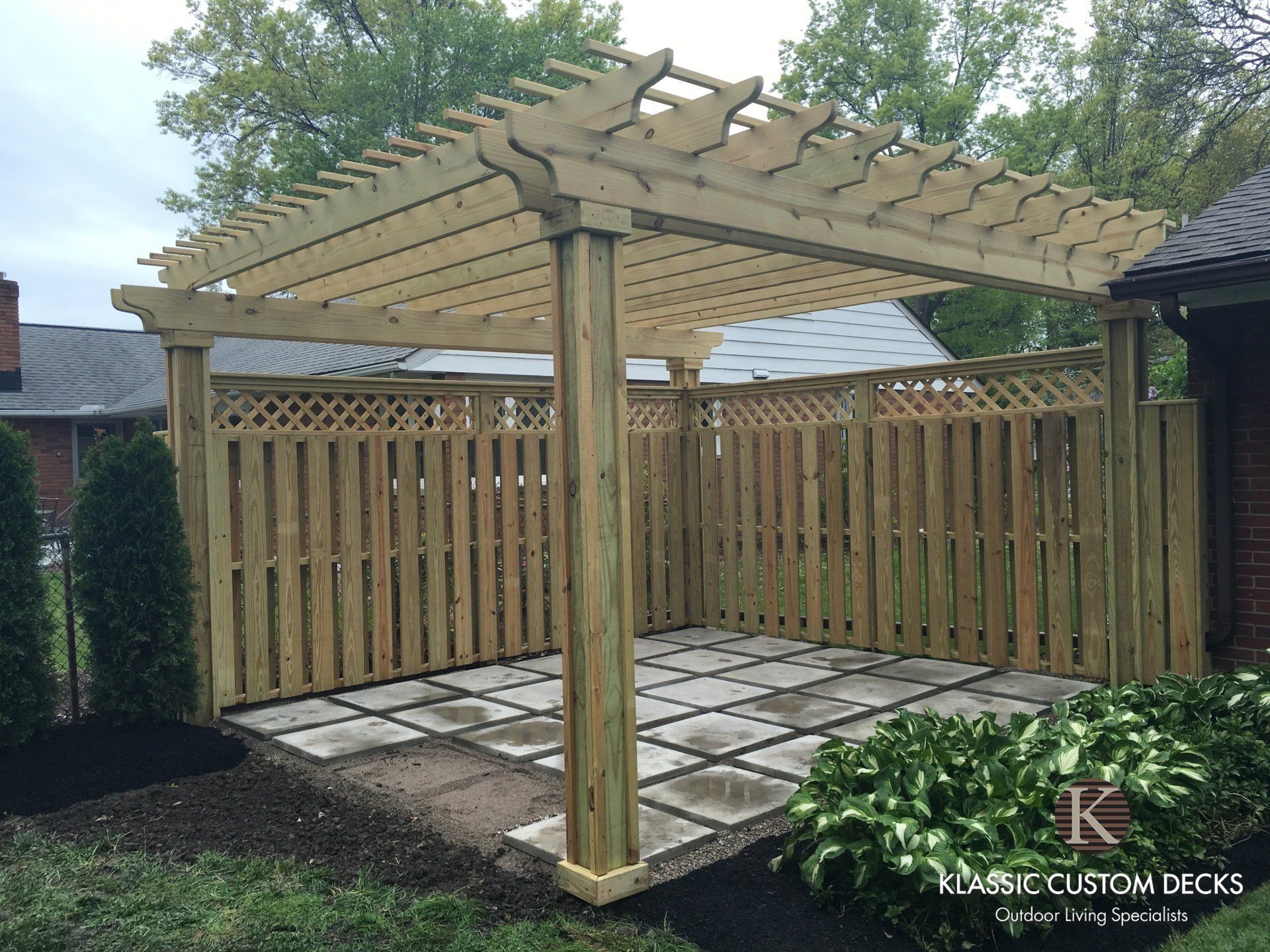 Wooden pergola and fenced patio with stone pavers in a landscaped backyard