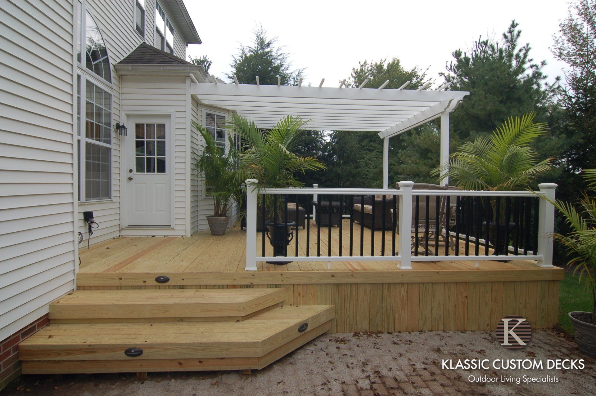 Backyard deck with wooden steps, white railing, and covered pergola beside a house.