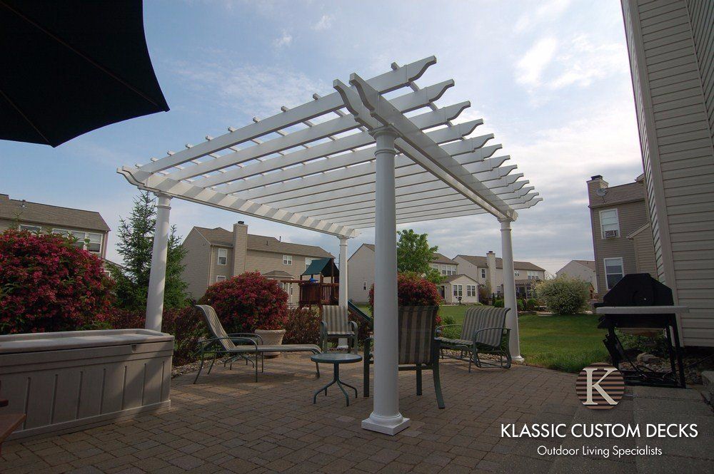 White pergola over patio dining set in a landscaped backyard with brick homes and greenery