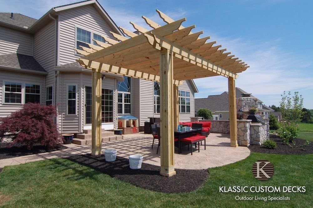 Backyard wooden pergola beside a house, with patio furniture and a landscaped yard