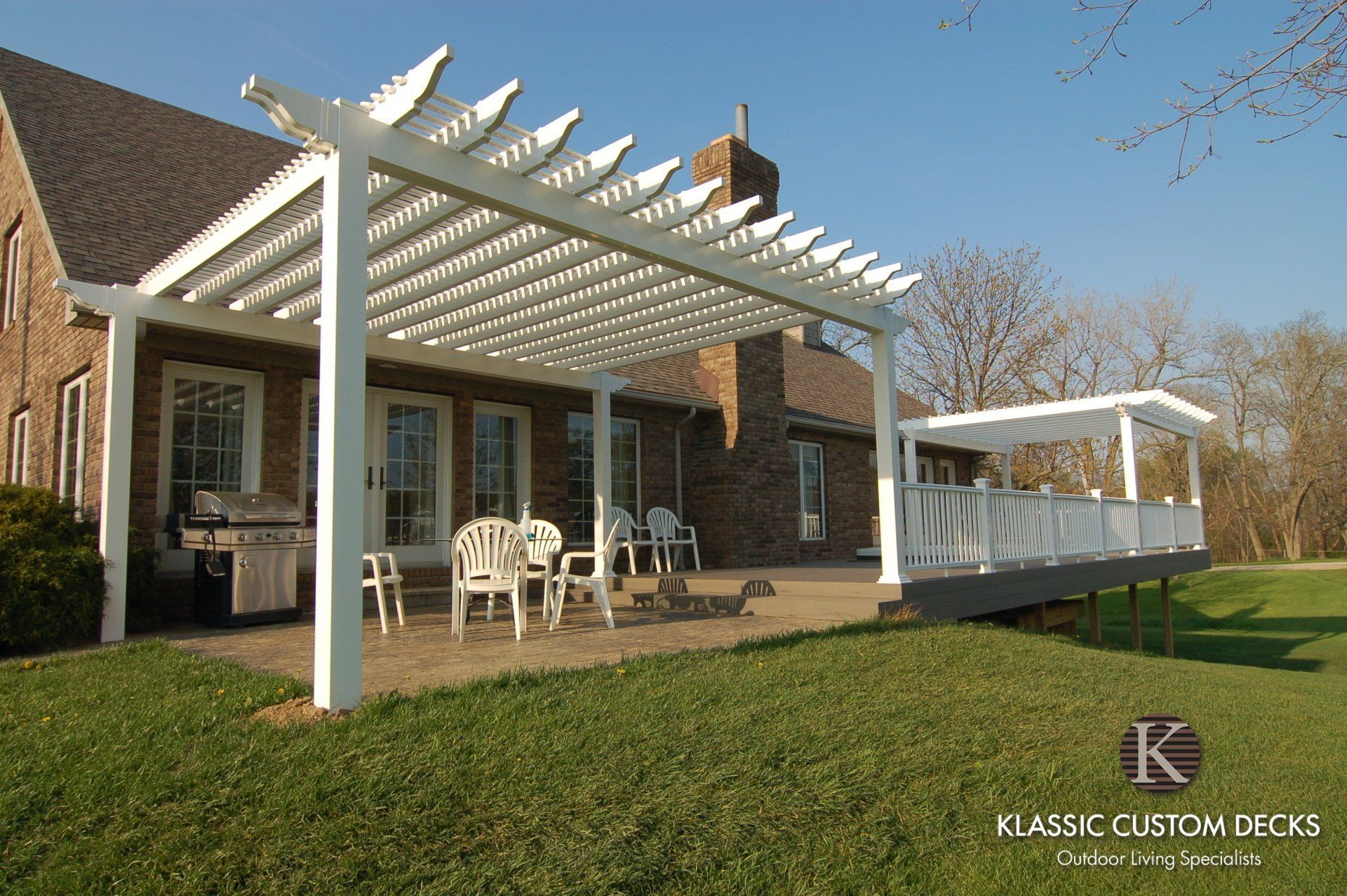 Backyard brick house with white pergola-covered patio and outdoor seating on a grassy lawn