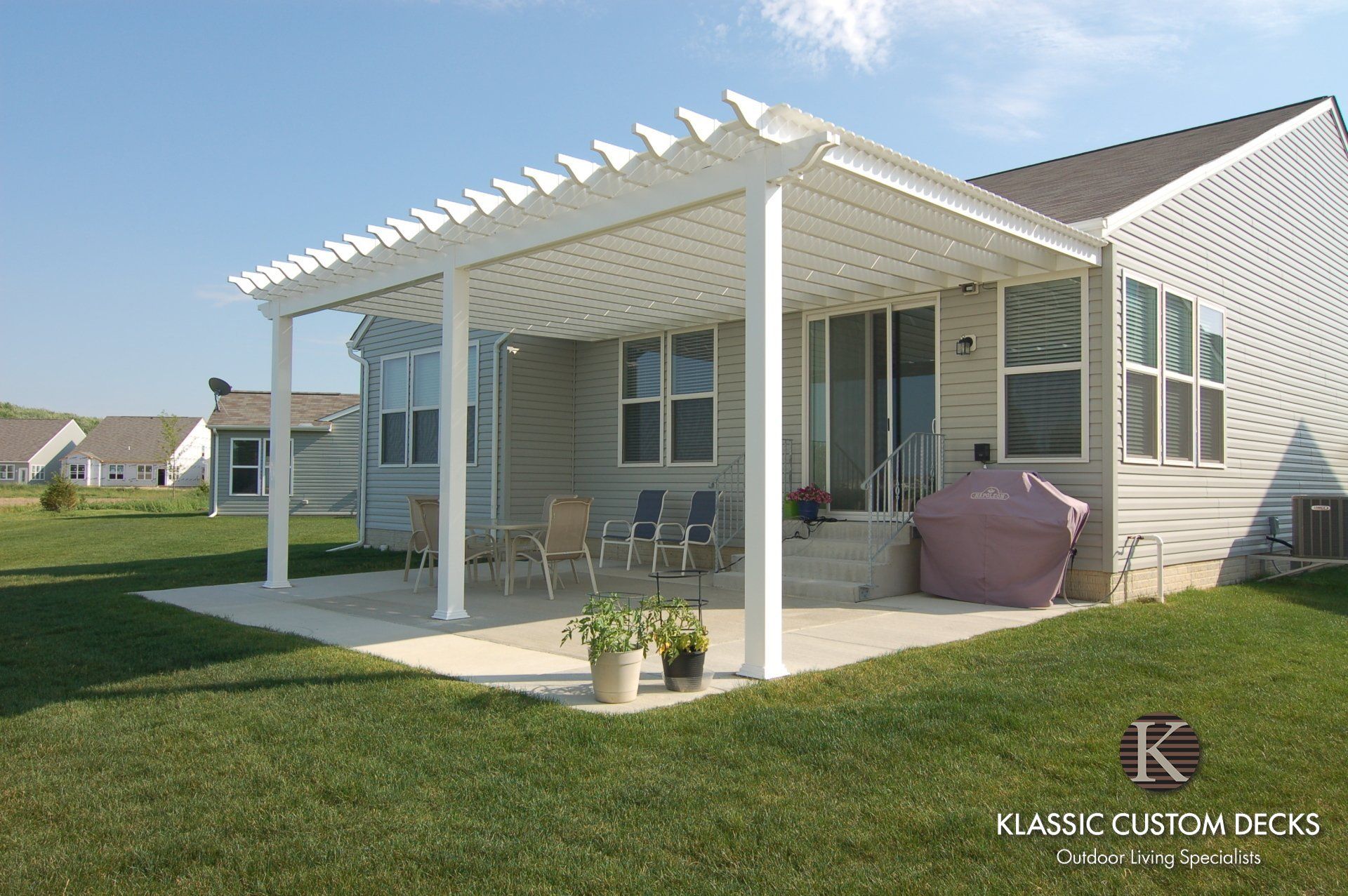 Backyard patio with white pergola, sliding doors, and a patio table and chairs on a green lawn