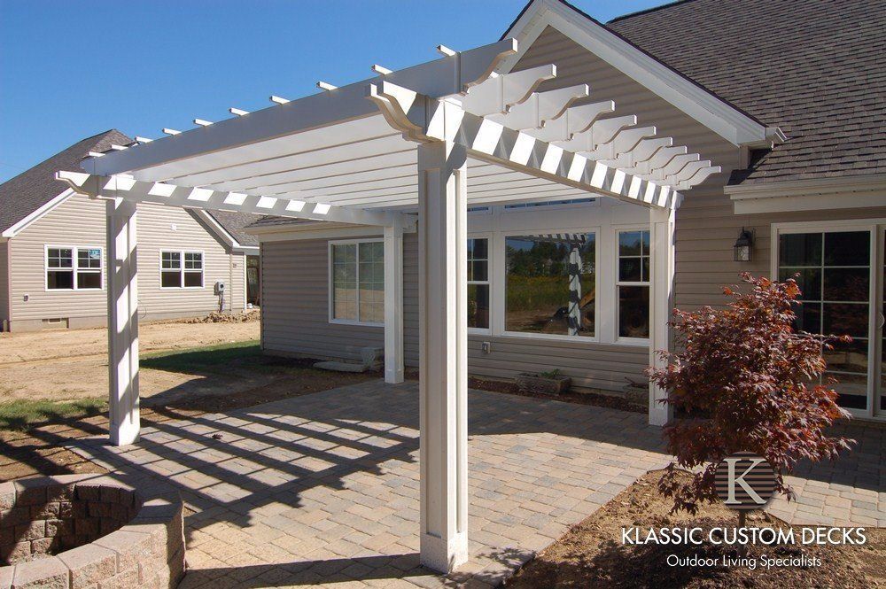 White pergola-covered patio attached to a house with brick pavers and backyard landscaping