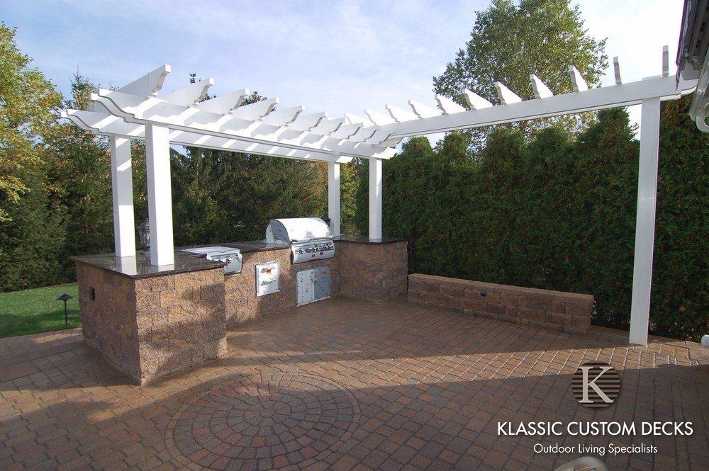 White pergola-covered outdoor kitchen with brick columns and built-in grill on a patio