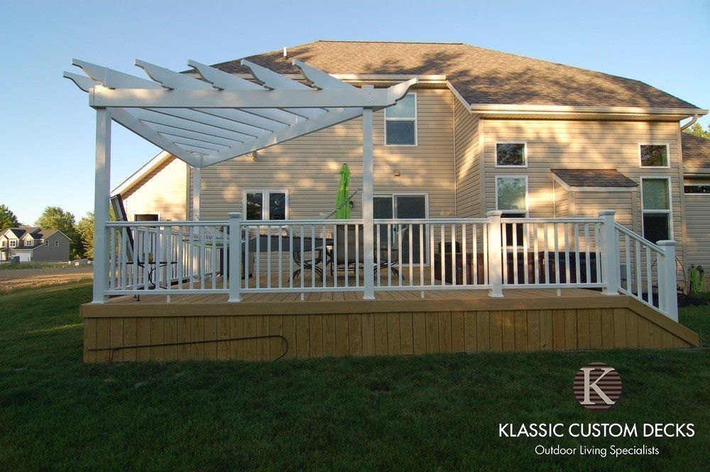 Backyard deck with white railing and pergola attached to a tan house at sunset