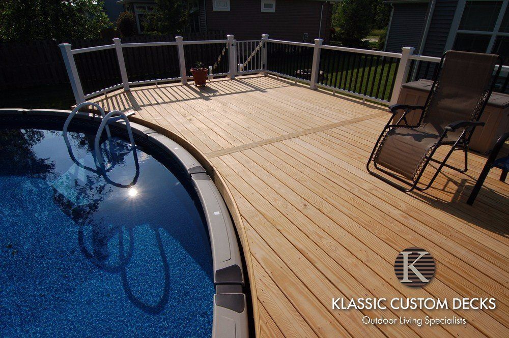 Curved blue pool beside a light wood deck with metal railing and lounge chairs in bright sunlight