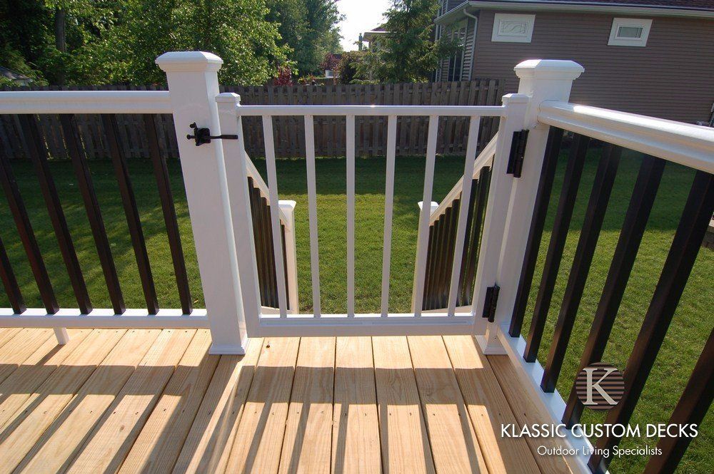White deck gate with vertical bars between railing posts, overlooking a backyard lawn.