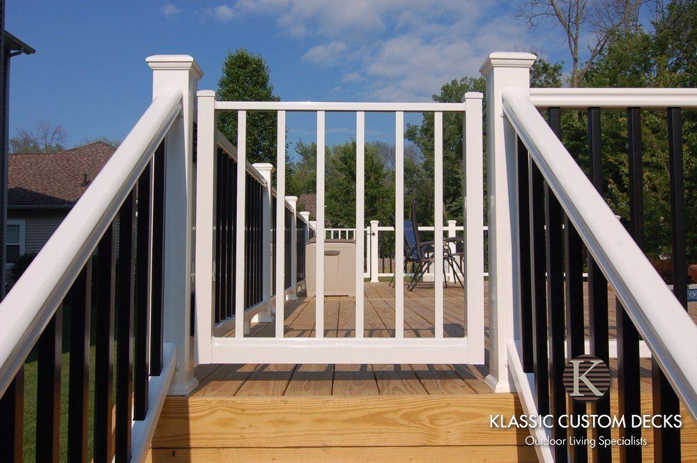 White deck railing and gate overlooking a backyard with a patio and trees under a blue sky