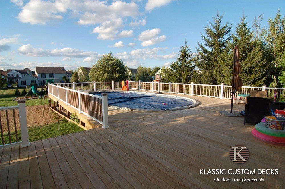 Wooden deck with round above-ground pool and white railings in a backyard under a blue sky