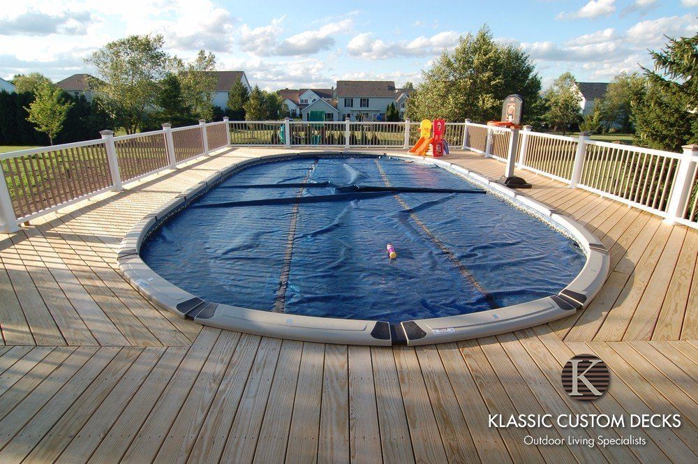 Above-ground pool with a blue cover on a wooden deck overlooking a backyard and trees