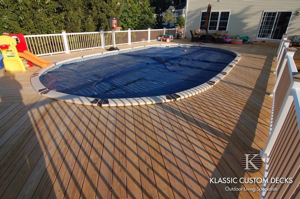 Wooden deck with a large blue-covered pool or hot tub in the center, surrounded by white railings.