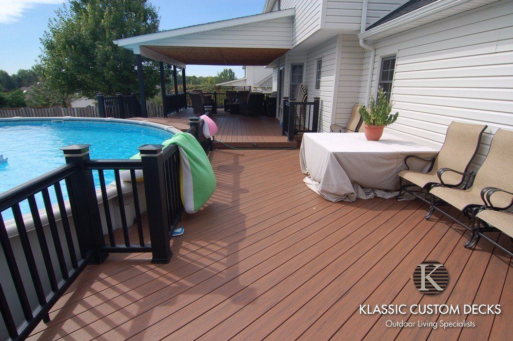 Poolside deck with white house siding, wooden railing, covered patio, and lounge chairs beside a blue pool