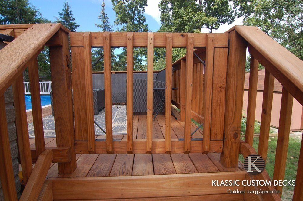 Wooden deck railing and stairs overlooking a backyard with a pool and trees