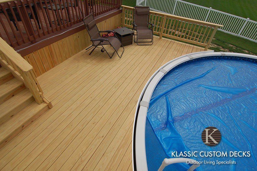 Wooden deck with blue-covered pool, lounge chairs, and railing overlooking a yard
