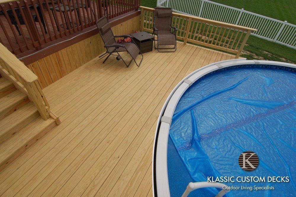 Wooden deck beside an above-ground pool, with patio chairs and railing.