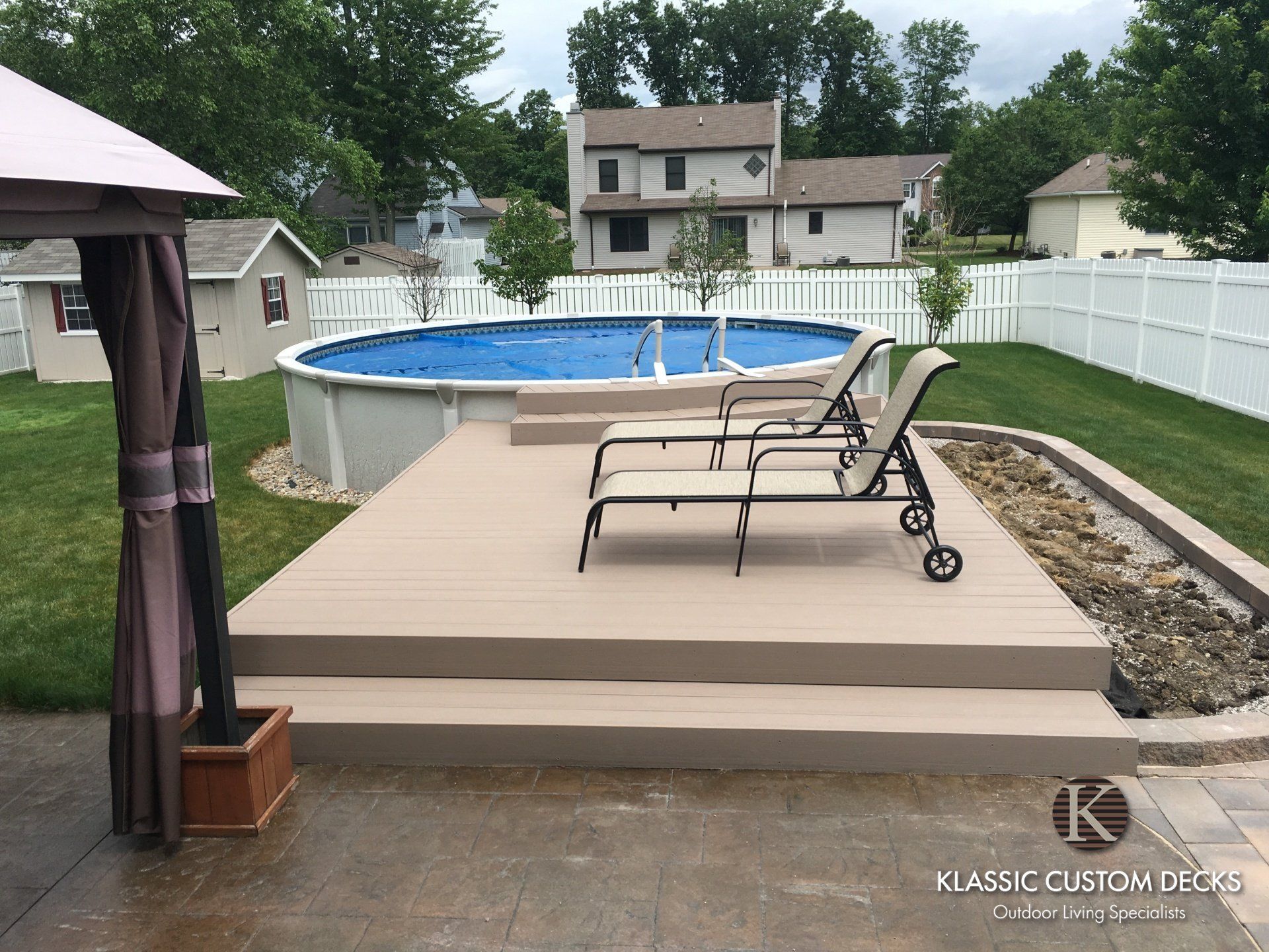 Backyard deck with lounge chairs beside an above-ground pool and white fence