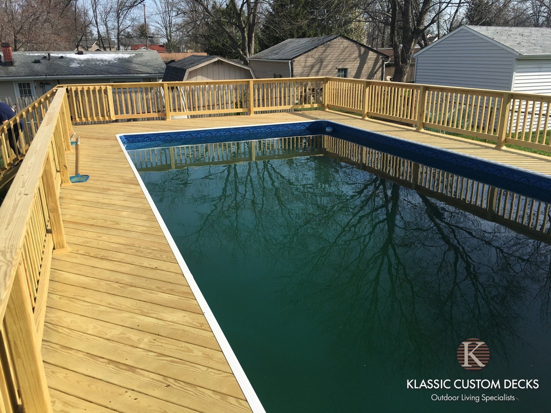 Wooden pool deck with railing around an in-ground pool in a backyard