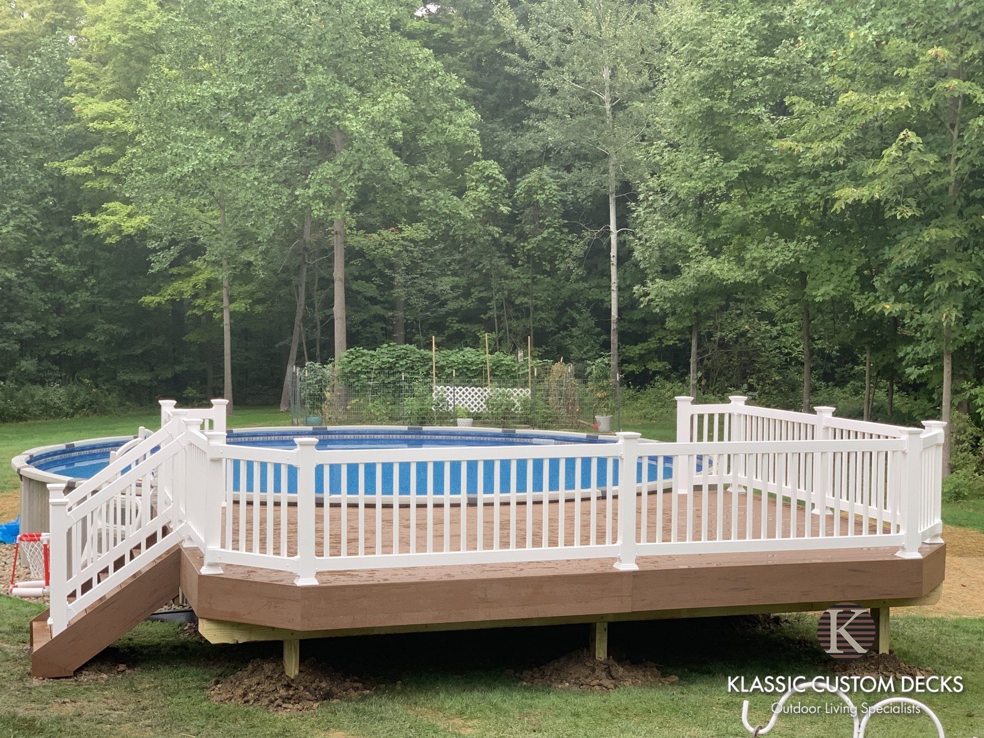 Round above-ground pool with white deck and railing in a wooded backyard