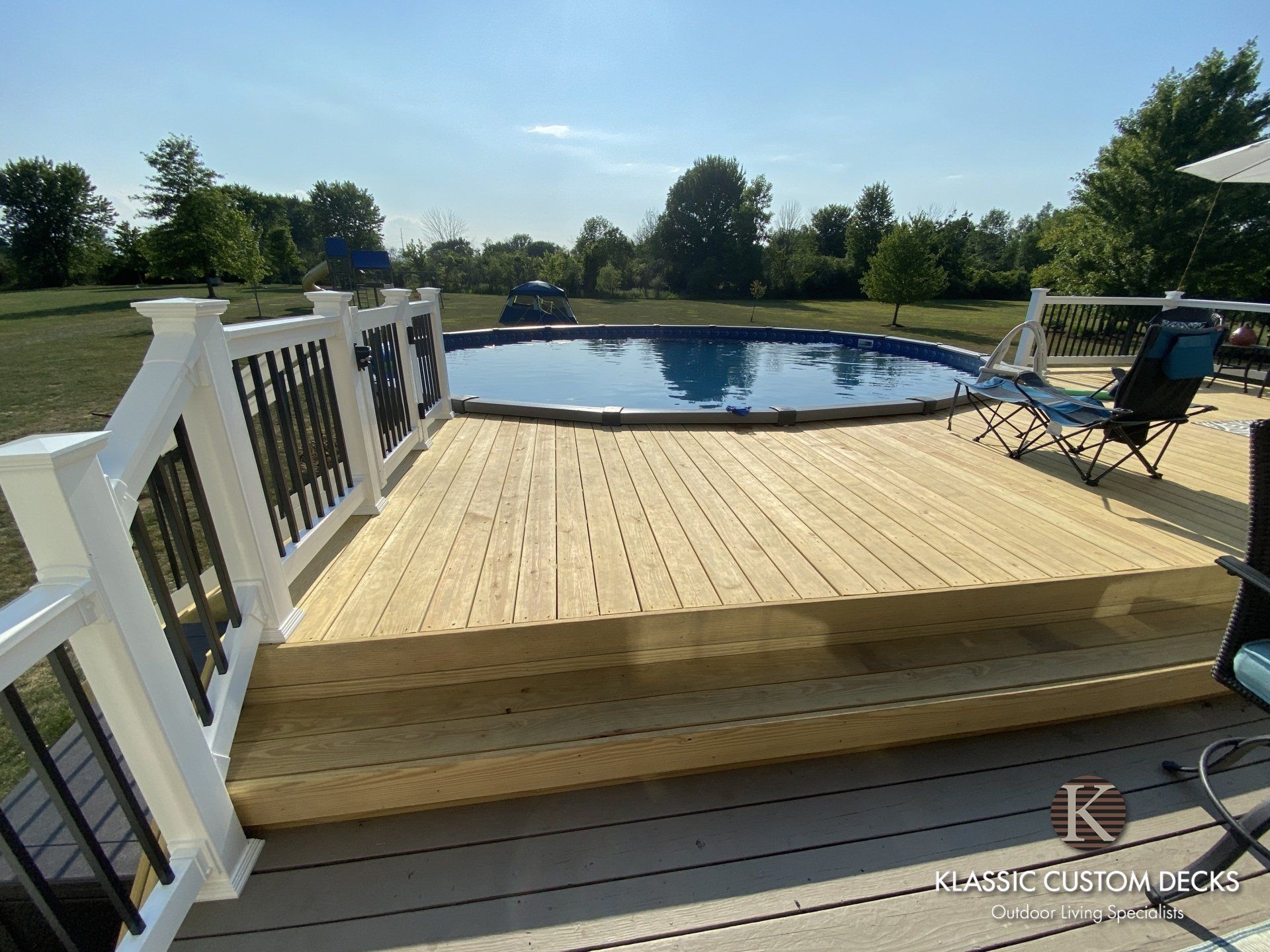 Wooden deck with white railing overlooking a swimming pool and grassy yard on a sunny day