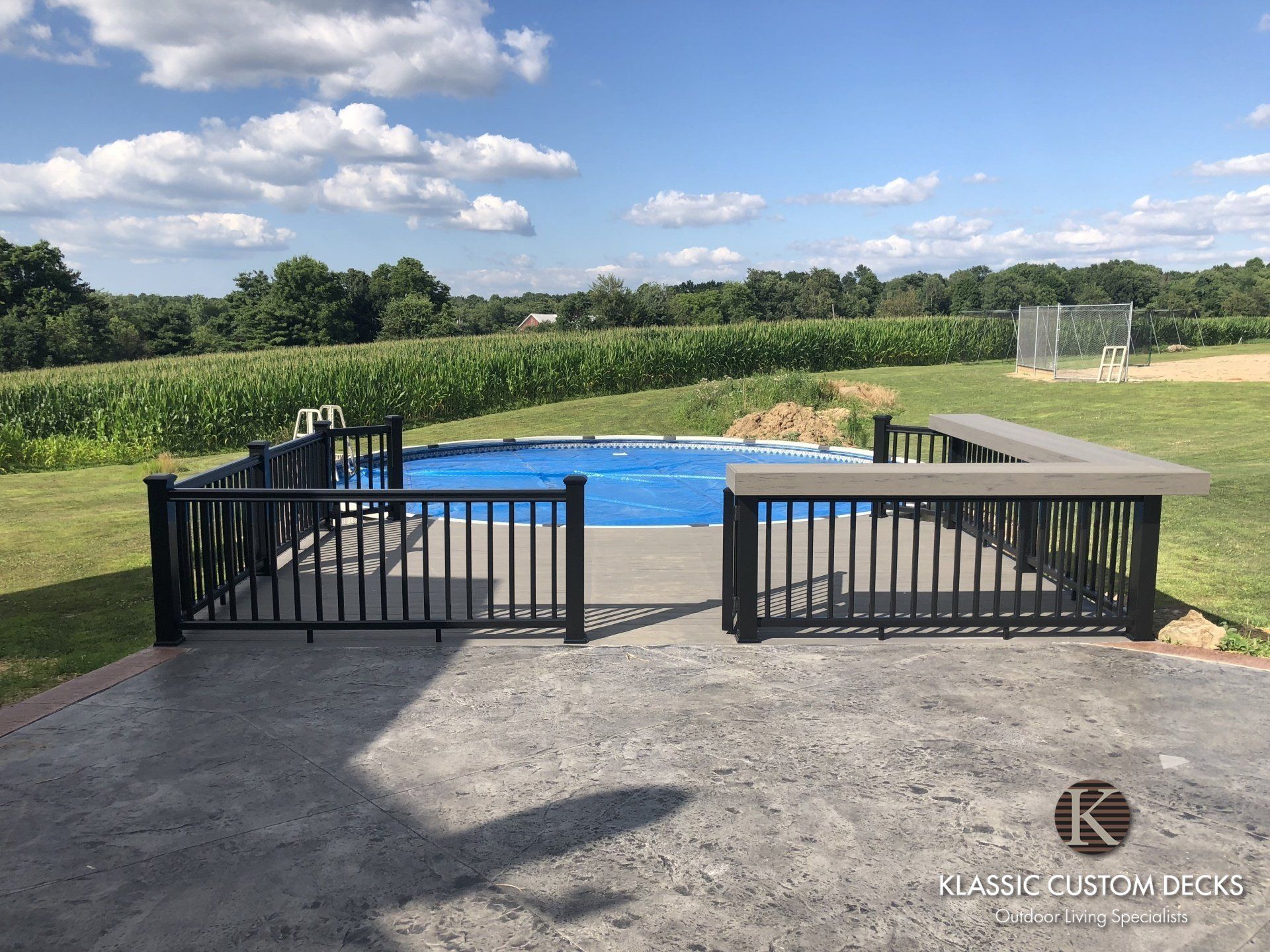 Backyard pool with black safety fences and a blue cover, bordered by lawn and hedges under a sunny sky