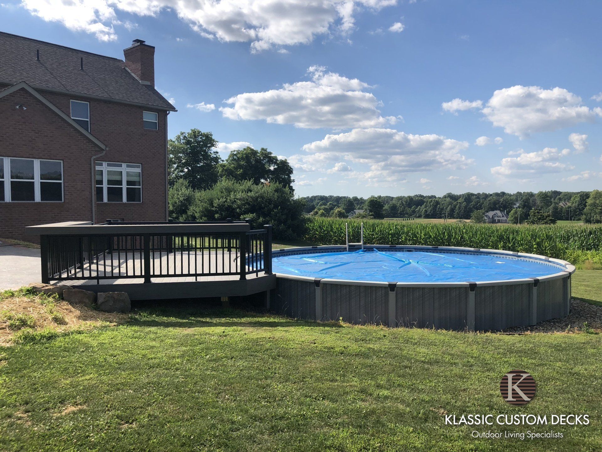Backyard above-ground pool beside a brick house under a sunny blue sky