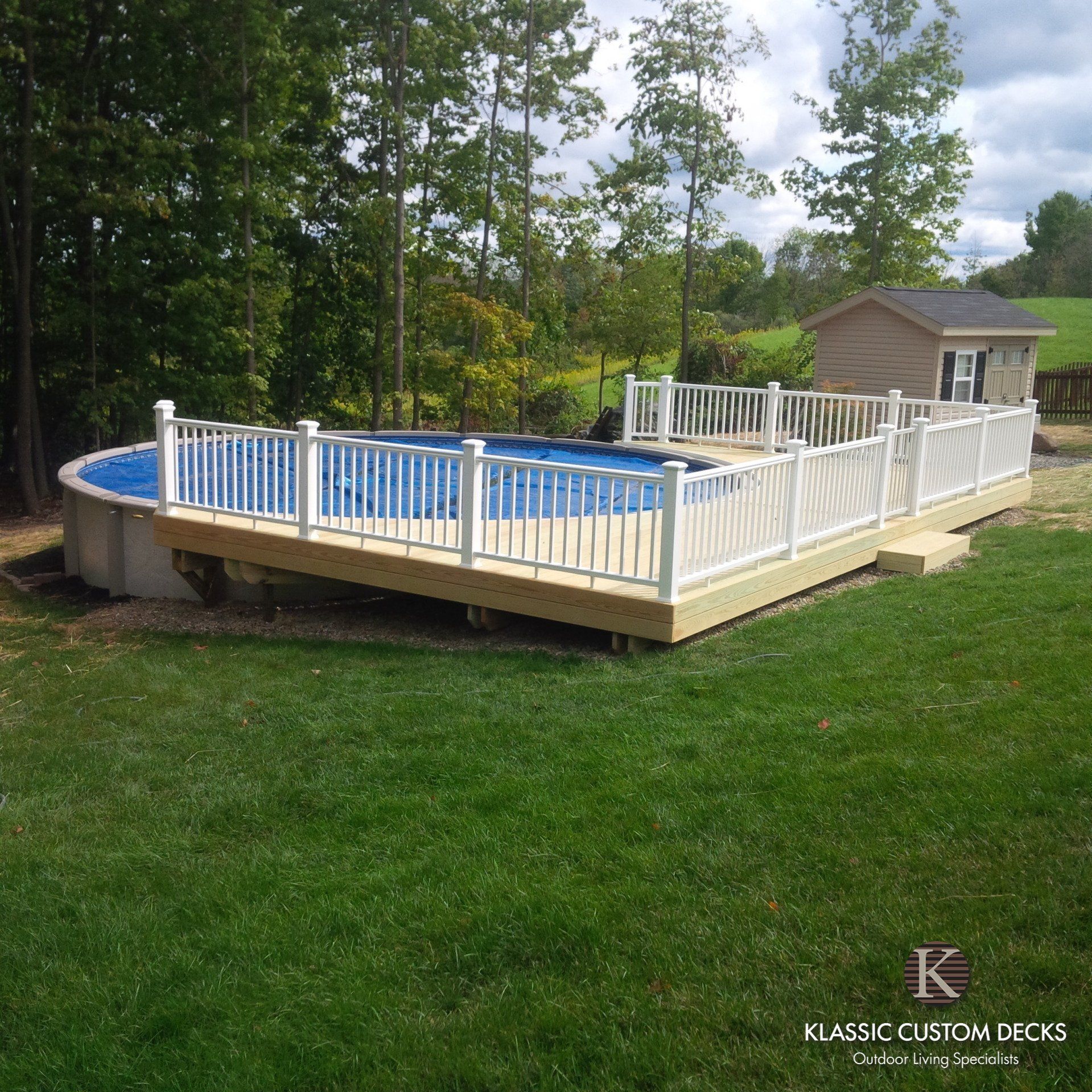 Raised above-ground pool deck with white railing beside a grassy yard and trees