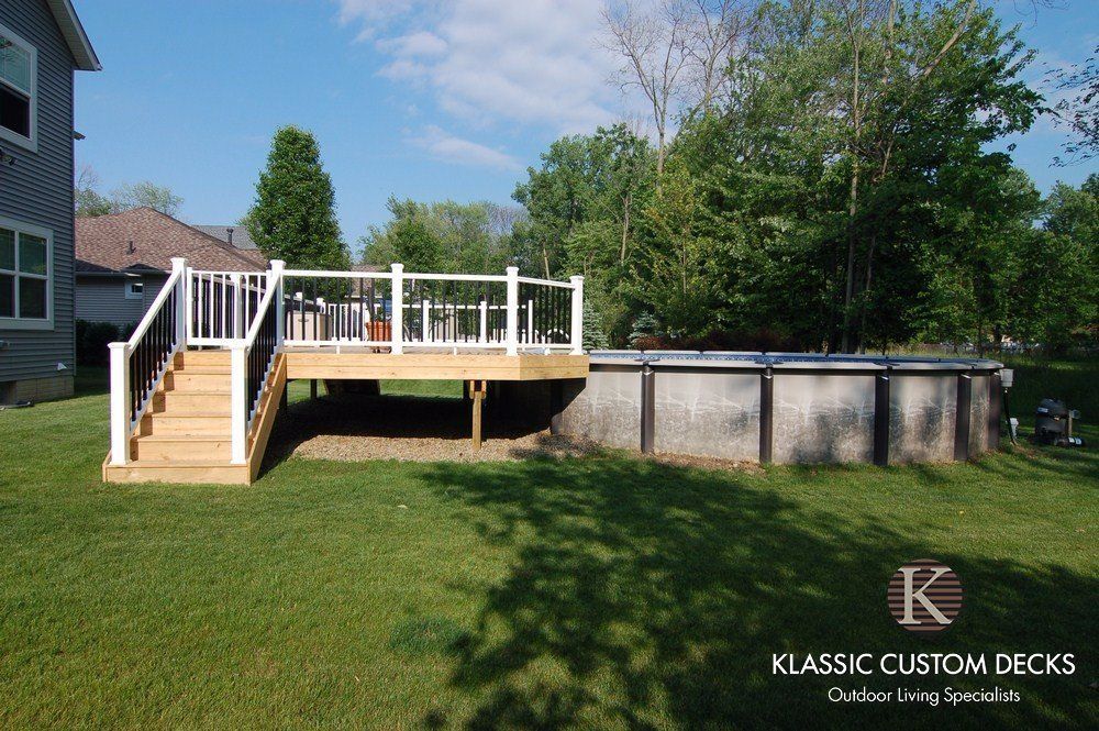 Backyard deck with white railings and stairs beside an above-ground pool under a blue sky