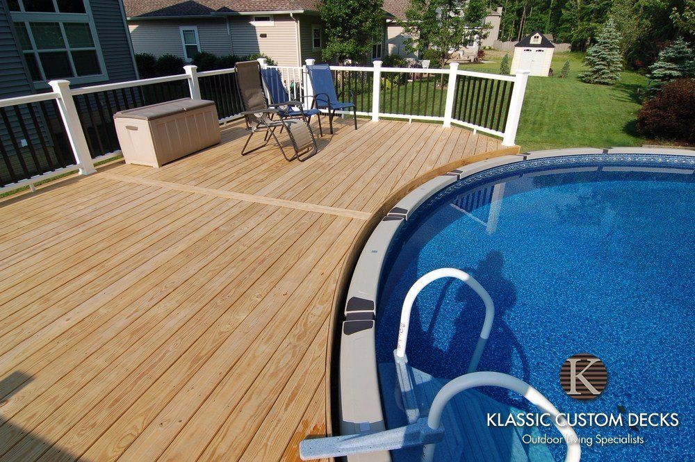 Wooden pool deck with lounge chairs beside a blue swimming pool and white railing