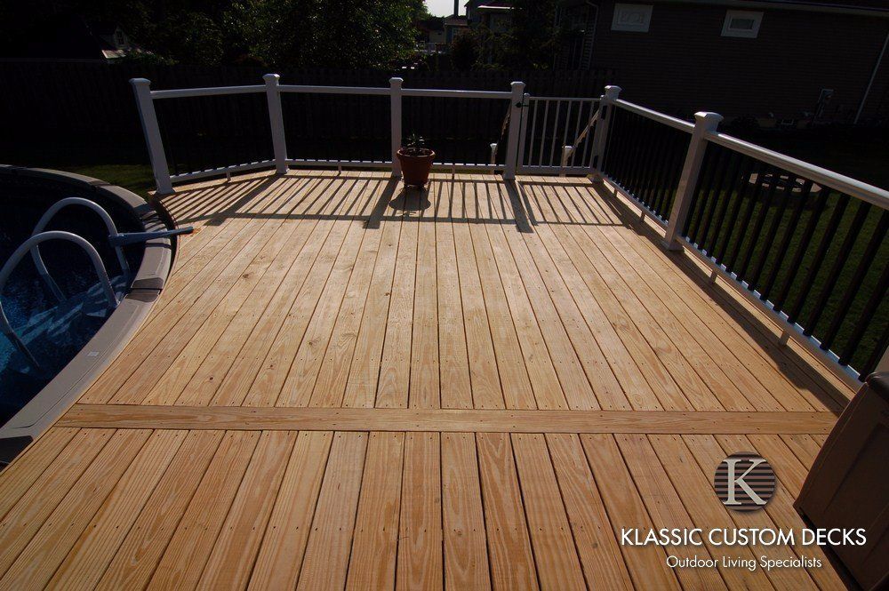Wooden deck with gray railing and a small dog standing in the center in sunlight.