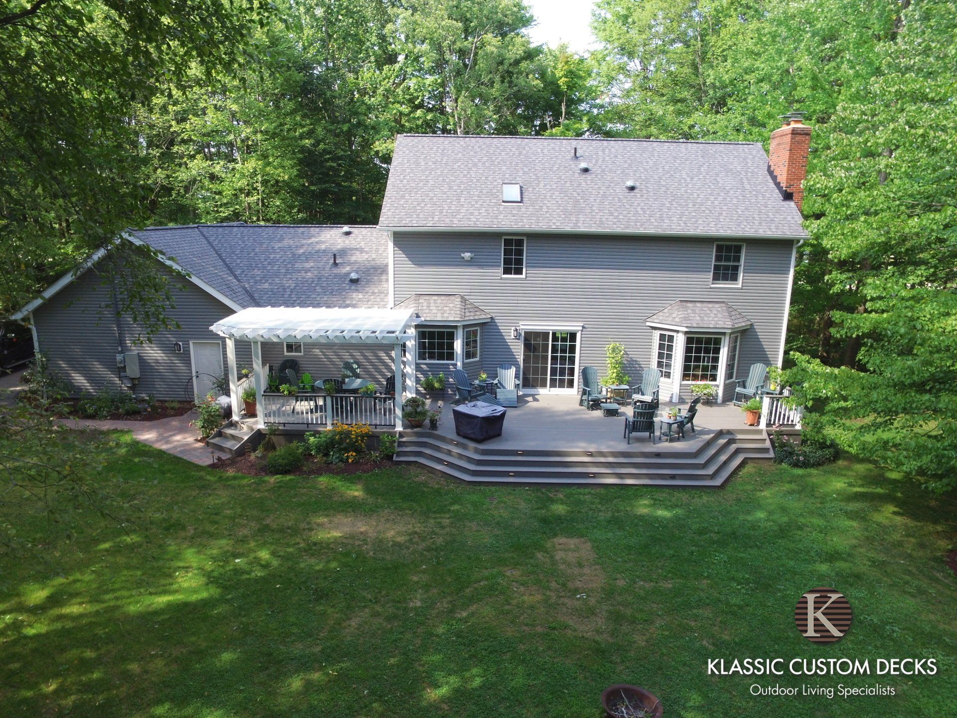 Two-story gray house with a large backyard deck, screened porch, and surrounding trees.