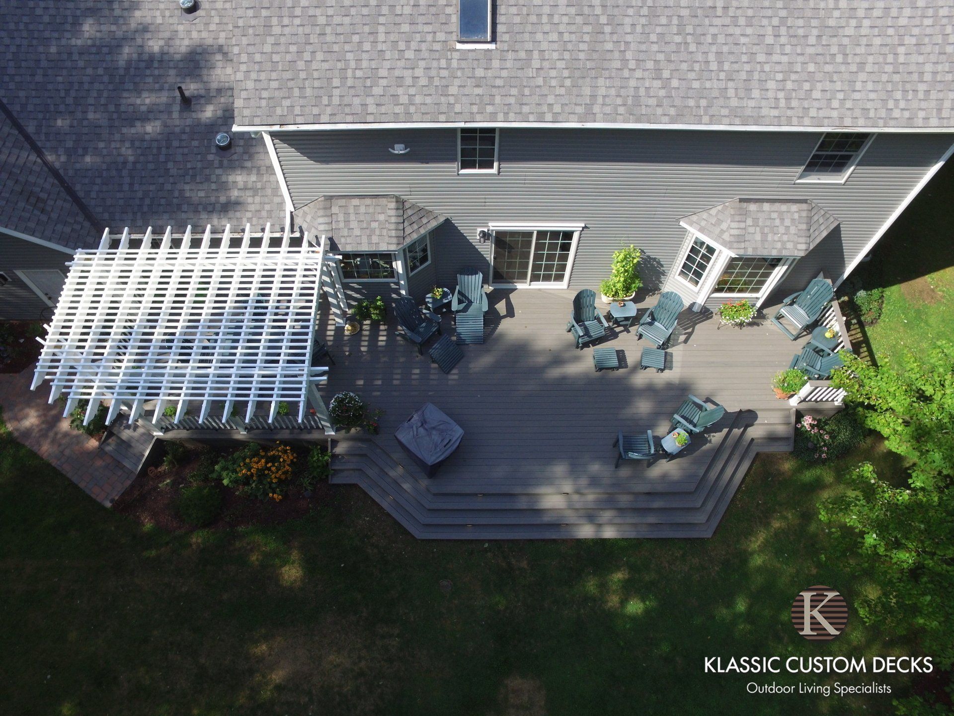 Aerial view of a backyard deck with white pergola, patio furniture, and house exterior.