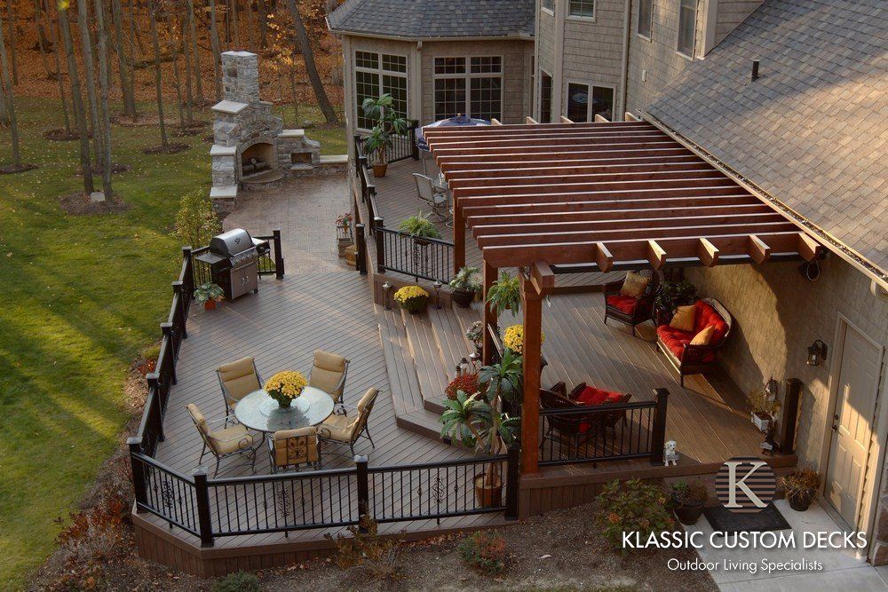 Backyard patio with a brown pergola, outdoor dining table, chairs, grill, and red hanging chairs by the house.