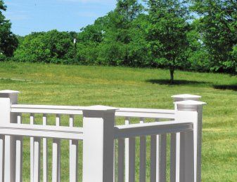 White porch railing overlooking a green lawn and trees on a sunny day