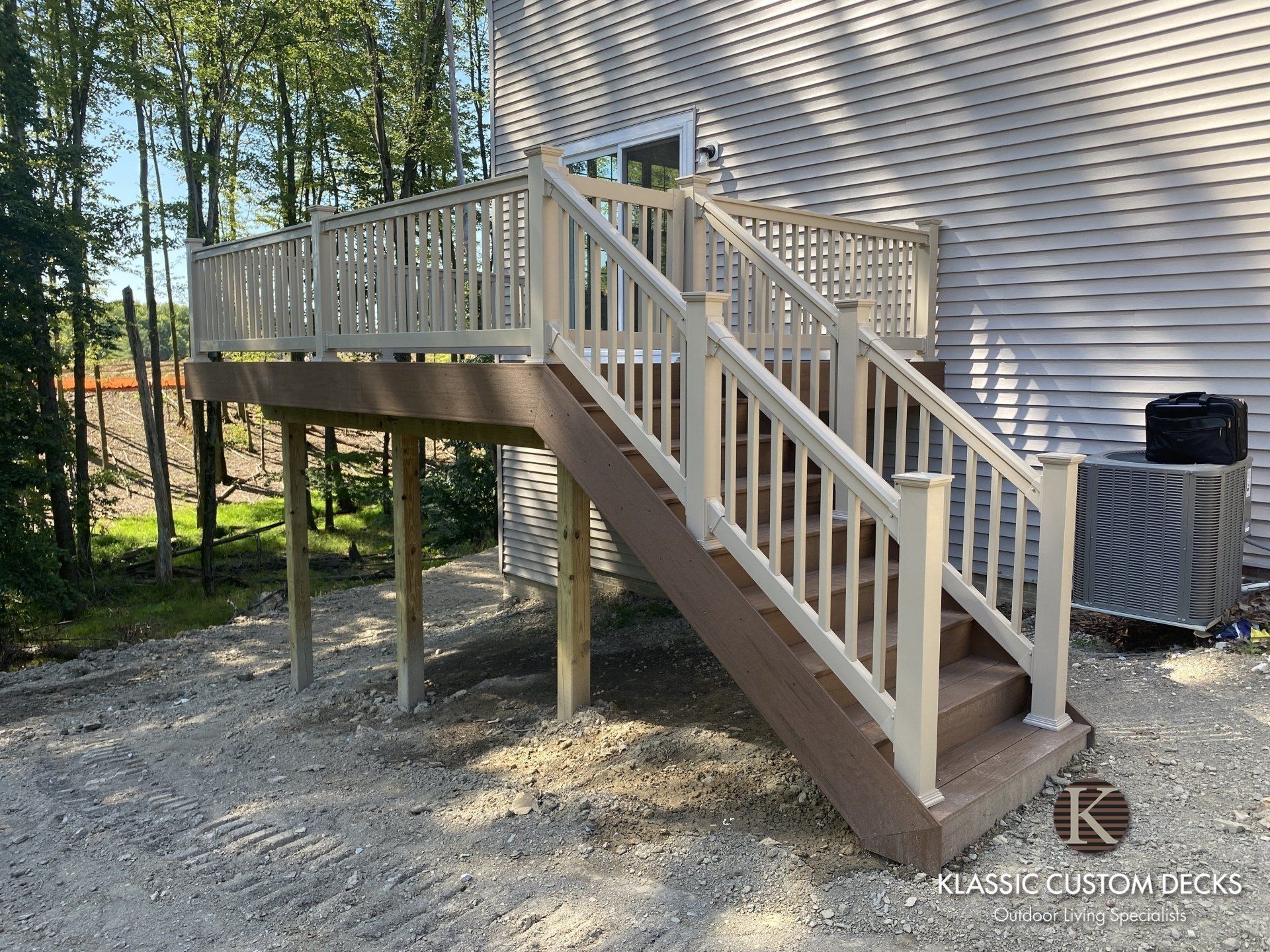 Raised wooden deck with stairs beside a house in a wooded yard