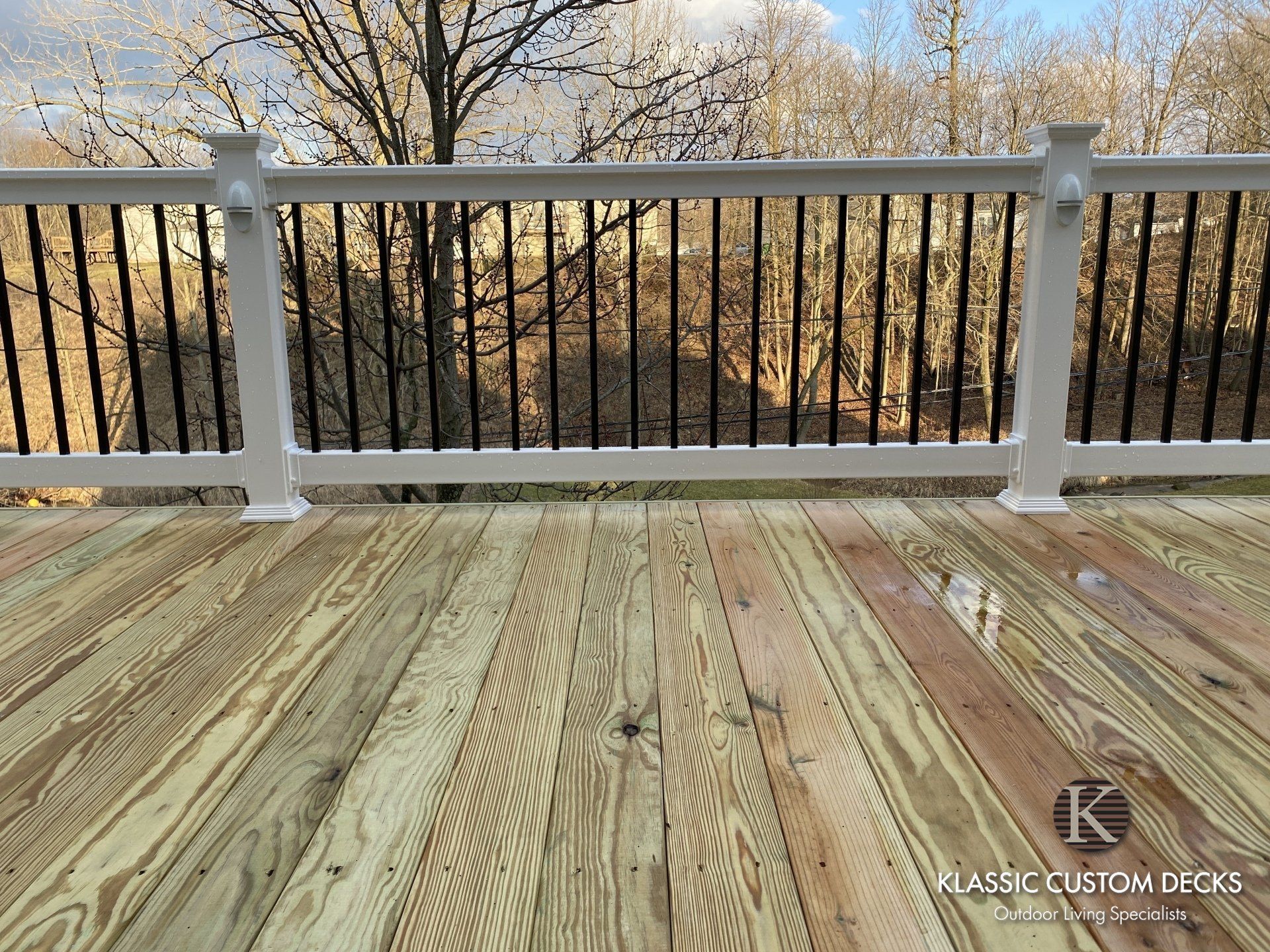 Wooden deck with white railing overlooking bare trees in a winter landscape