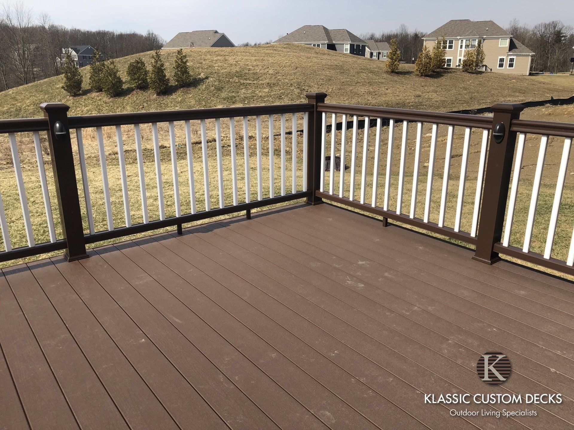 Wooden deck with dark railings overlooking a grassy backyard and suburban houses.