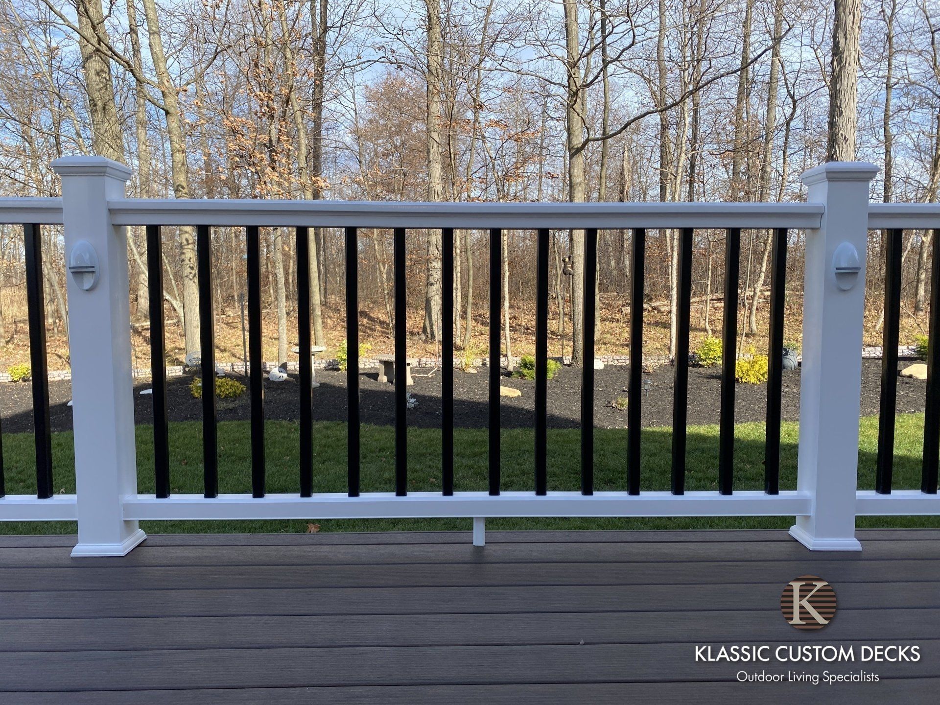 White porch railing with black balusters overlooking a wooded yard in autumn