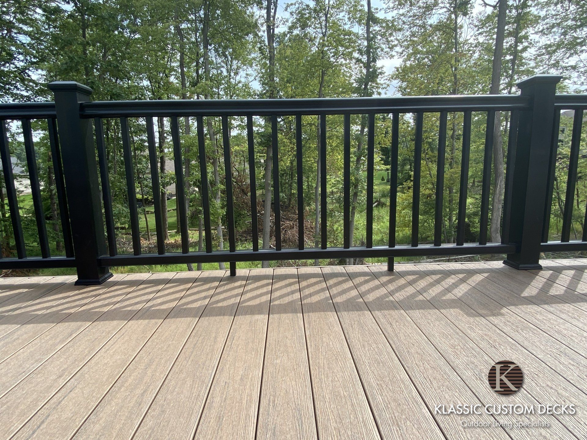 Black railing on a wooden deck overlooking green trees and shrubs
