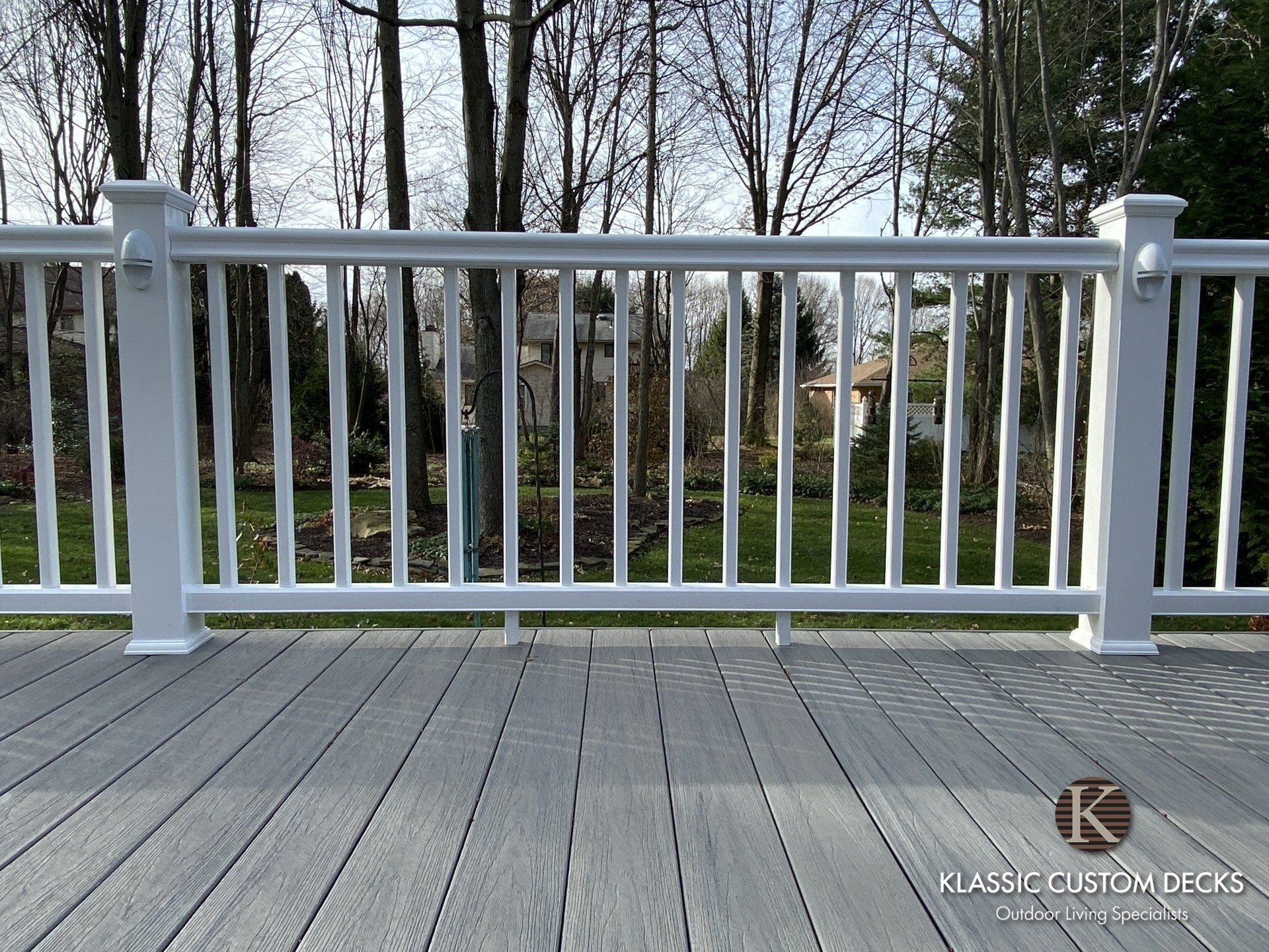 White railing on a gray wooden deck with trees and lawn in the background